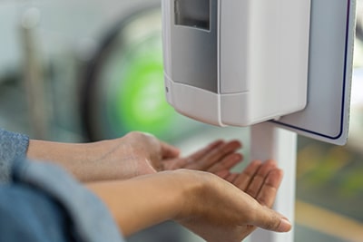 Woman Holding Hands Under Automatic Sanitizer Dispenser